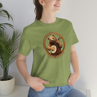 A woman wearing a green banjo shirt with a brown bear smiling while holding a banjo framed by a circular banjo head with the word "clawhammer" beneath.