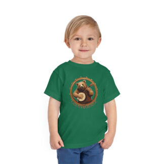 A little boy wearing a green banjo shirt with a brown bear smiling while holding a banjo framed by a circular banjo head with the word "clawhammer" beneath.